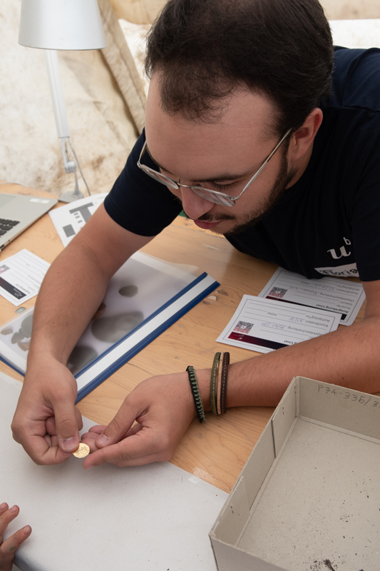 Student und Expert, der einem kleinen Archäologen erklärt, was er gefunden hat. Er hält eine Münze in der Hand.