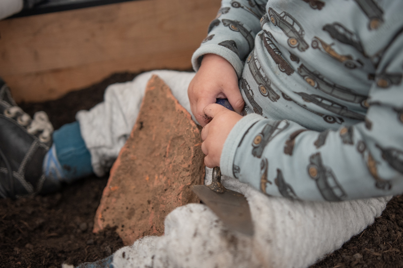 Baby mit Fundstück (Ziegel) zwischen den Beinen.